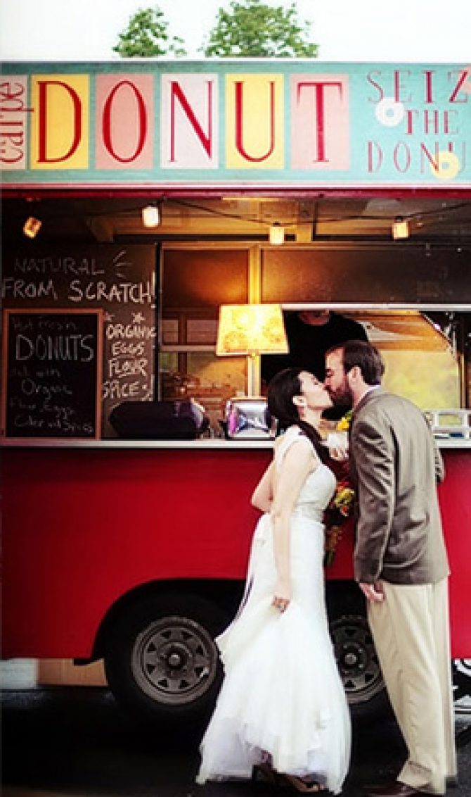 A newlywed couple shares a romantic kiss in front of a donut truck on their special day.