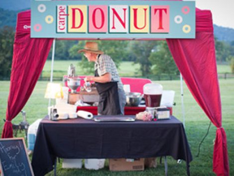 A man selling donuts under a tent in a field.