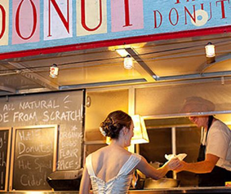 A woman is standing in front of a donut truck.