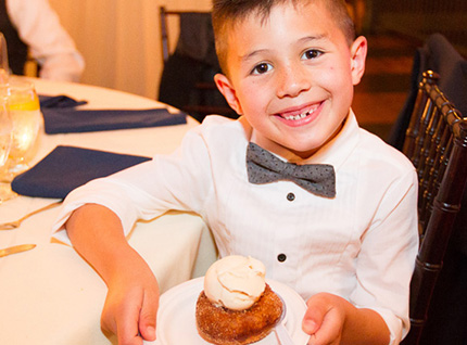 A young boy joyfully holds a delicious dessert in his hands, savoring the sweet treat with delight.
